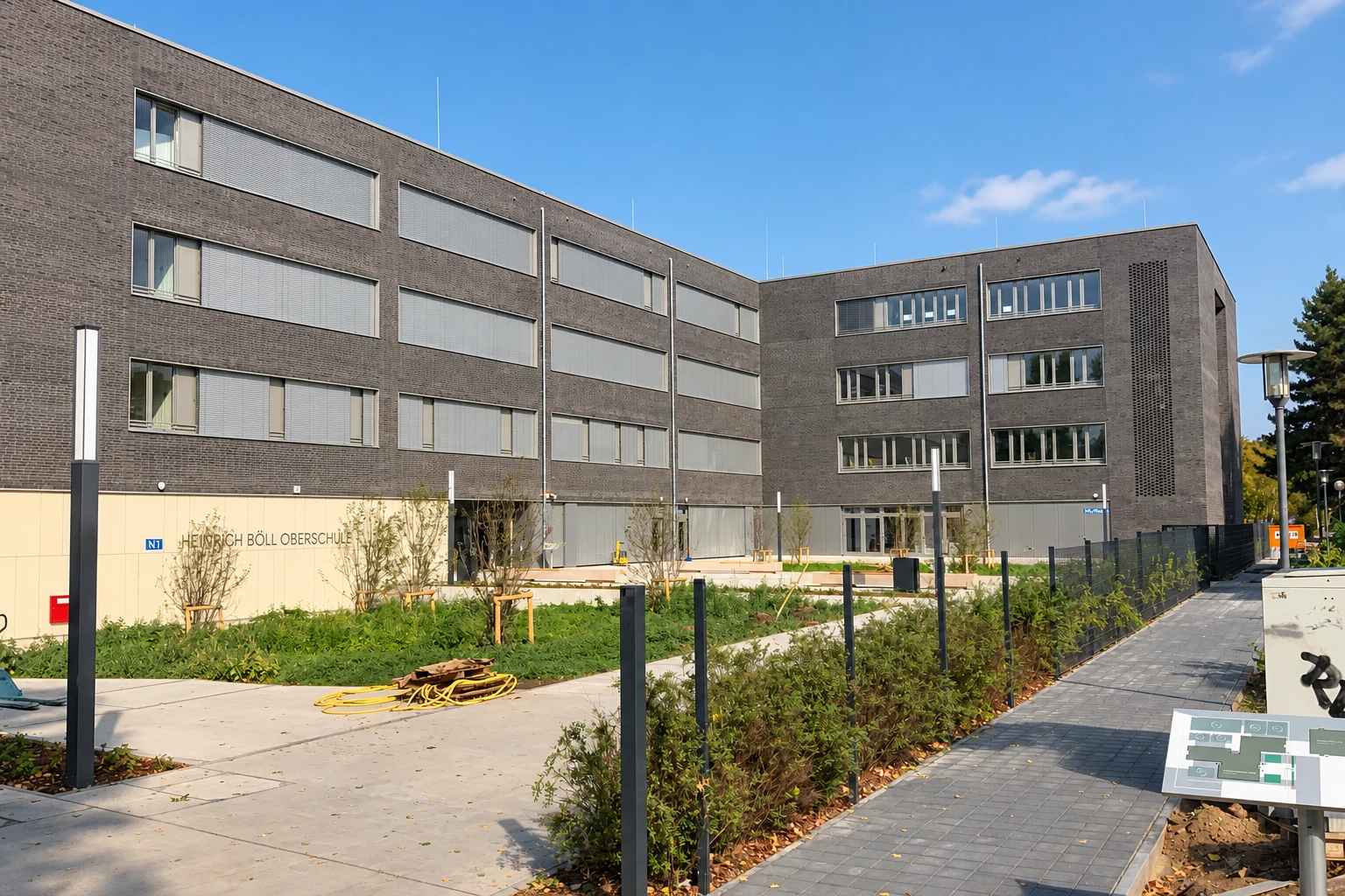 Mehrgeschossiges Gebäude mit grauer Klinkerfassade und begrüntem Vorplatz – Archivaufnahme